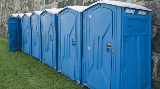 Row of blue portable toilets lined up on grass against a stone wall for event sanitation in Anchorage, AK