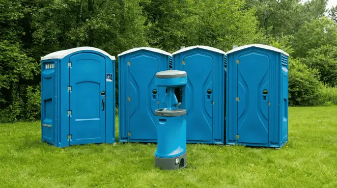 Four blue portable toilets and a matching hand washing station on grass near trees, a common sight at local outdoor events in Anchorage, AK