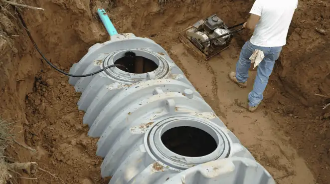 Septic tank installation showing a technician compacting soil around a new poly septic tank in an excavation pit in Anchorage, AK
